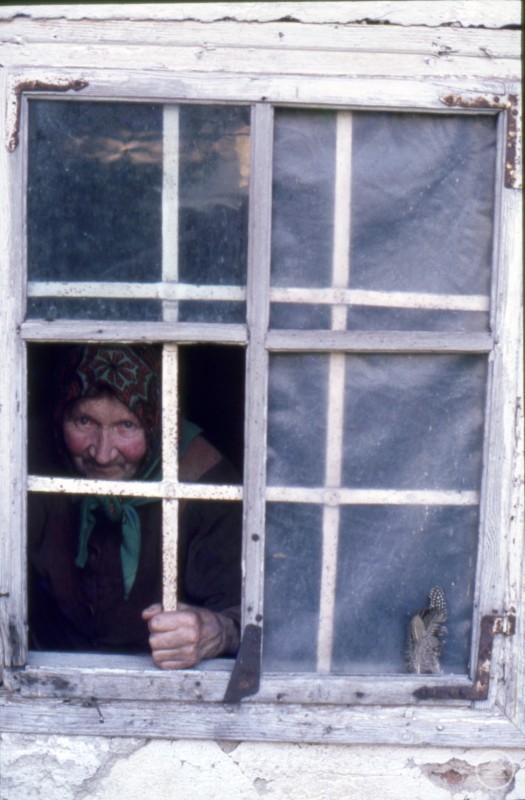 Karolina Graf im Jahr 1978 Frau schaut aus altem Fenster und hält Eisenstange der Vergitterung des Fensters in der Hand.