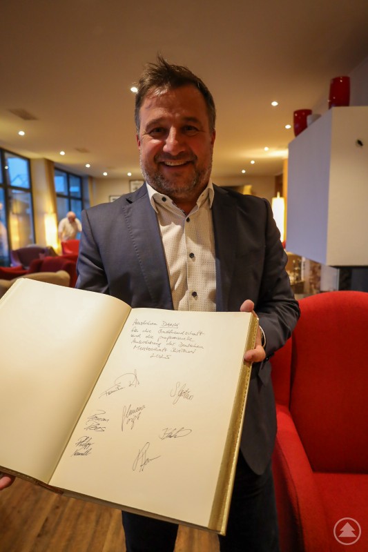 Bürgermeister Karl-Heinz Eppinger präsentiert stolz die Unterschriften der deutschen Biathlon-Nationalmannschaft im Goldenen Buch der Glasstadt. Ein Mann im Anzug hält das Goldene Buch der Stadt Zwiesel offen und zeigt die handschriftlichen Einträge und Unterschriften der Biathleten.