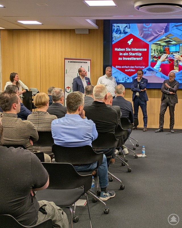 Diskussionsrunde zum Thema Wagniskapital und StartUp-Investments bei einer Veranstaltung in Passau. Mehrere Referenten stehen vor einem sitzenden Publikum in einem Veranstaltungsraum. Auf einer großen Präsentationswand wird eine Folie zum Thema Investitionen in StartUps gezeigt. Die Zuhörer verfolgen eine Podiumsdiskussion in konzentrierter Atmosphäre.