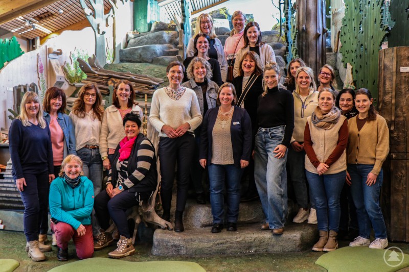 Freuten sich über ein weiteres gelungenes Jahr der Zusammenarbeit: Die Vertreterinnen der Nationalpark-Kindergärten, Nicole Graf-Kilger und Lisa Keilhofer von der Nationalparkverwaltung und die ehrenamtlichen Waldführerinnen. Auch Nationalparkleiterin Ursula Schuster (Mitte) ließ sich das Jahrestreffen nicht entgehen. Gruppenfoto mit rund 20 Frauen im Hans-Eisenmann-Haus, darunter Vertreterinnen der Nationalpark-Kindergärten, Mitarbeiterinnen der Nationalparkverwaltung und ehrenamtliche Waldführerinnen, aufgenommen vor einer naturnah gestalteten Kulisse mit Holz, Felsen und Pflanzen.