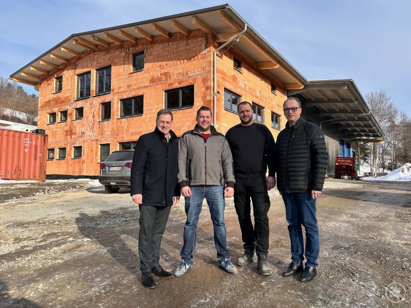 Bürgermeister Alexander Mayer (v.l.), Tobias Lippl, Markus Faltermeier und MdL Martin Behringer vor der LiFa-GmbH-Zentrale, die im Rekordtempo realisiert wurde. Vier Männer stehen bei winterlichen Bedingungen vor einem modernen, noch unverputzten Büro- und Hallengebäude. Die Sonne scheint, im Hintergrund liegt Schnee.