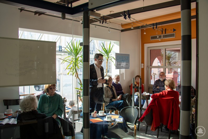 Einfühlsamer Austausch - OB Dr. Moser beim Begegnungsnachmittag für Verwitwete Mehrere ältere Menschen sitzen in einem Café an Tischen bei Kaffee und Kuchen, während Oberbürgermeister Dr. Christian Moser im Gespräch steht.