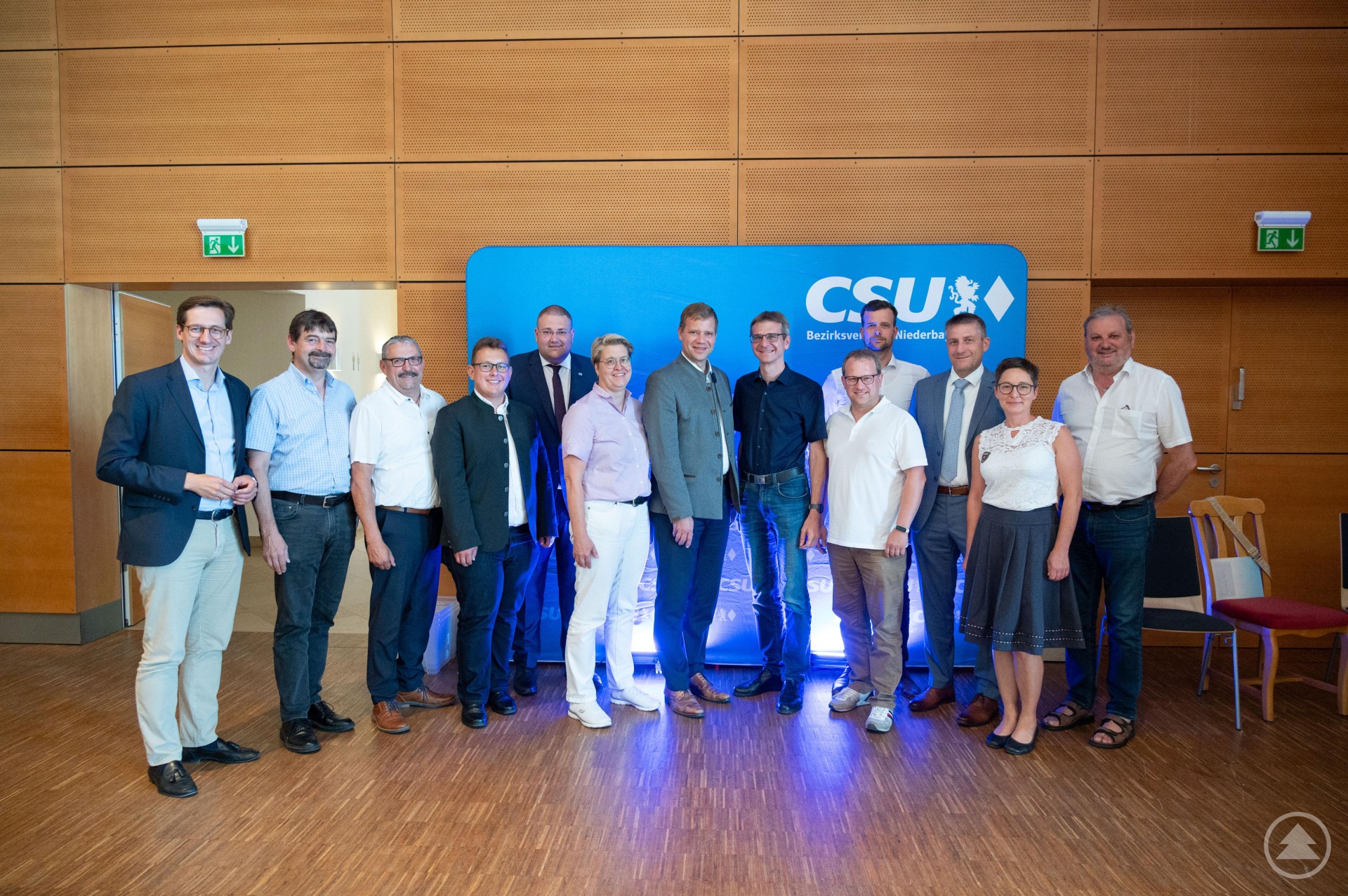 Eine Gruppe von CSU-Delegierten aus dem Kreisverband Freyung-Grafenau steht dicht beieinander bei einer Veranstaltung, einige tragen Namensschilder. Im Hintergrund ist ein Rednerpult zu erkennen.
