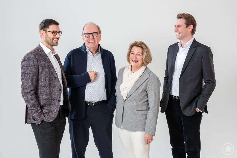 Die Familie Graf führt das Unternehmen inzwischen in dritter Generation und verbindet Tradition mit neuen Ideen. Vier Personen aus der Unternehmerfamilie stehen gemeinsam vor neutralem Hintergrund und unterhalten sich. Sie repräsentieren die nächste Generation im Familienunternehmen.