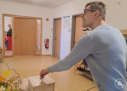 Ein Mann wirft einen Wahlzettel in eine kleine Wahlurne in einem Gemeinschaftsraum.