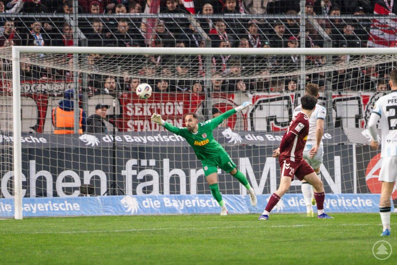 Torwart des SSV Jahn Regensburg in gr&uuml;nem Trikot fliegt bei einem Elfmeter spektakul&auml;r in die Ecke und pariert den Ball vor dem Tor.