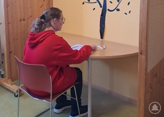 Eine junge Frau sitzt an einem Tisch in einer kleinen Nische und f&uuml;llt ihren Stimmzettel aus.