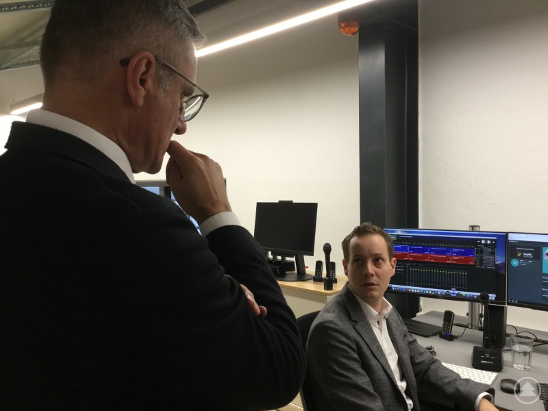 Daniel Pröbstl, Projektleiter beim Bayerischen Zentrum für besondere Einsatzlagen, zeigt MdL Muthmann am Leitstand, wie Videokameras und Mikrofone alle Bewegungen aufzeichnen.