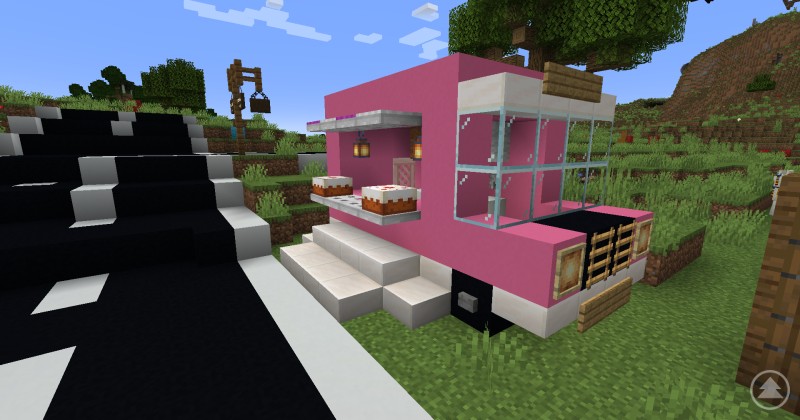 Mobiler Imbisswagen mit Kuchenauslage in der Minecraft-Smart World des Ilzer Landes. Ein pinkfarbener Verkaufswagen in Minecraft mit zwei Kuchen auf einer Theke, Laternenbeleuchtung und Treppenaufgang.