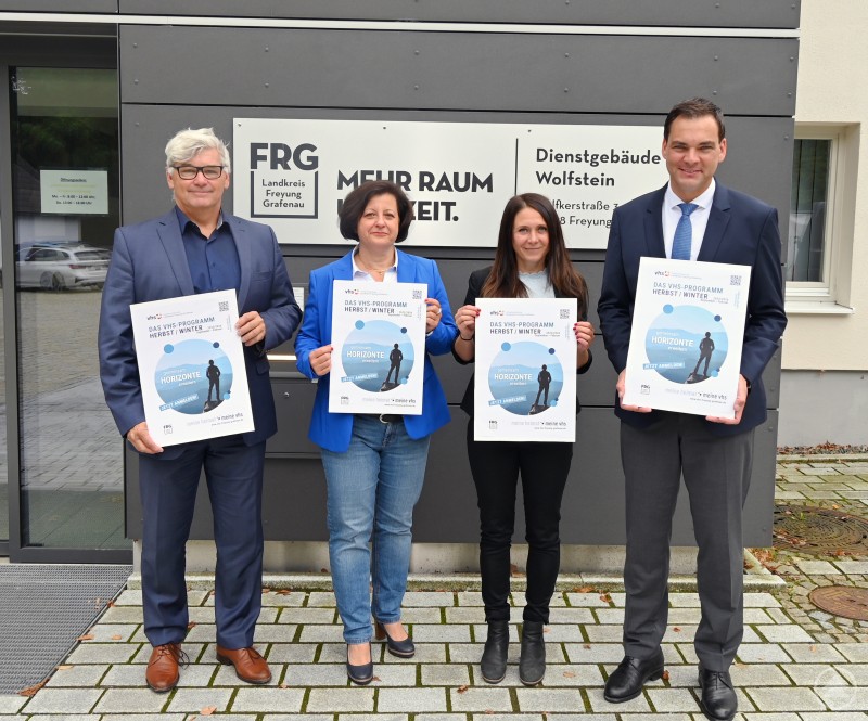 Offizielle Vorstellung des neuen vhs-Programms für den Landkreis Freyung-Grafenau (v.l.): Siegfried Wilhelm, Klara Köck, Dr. Karina Fisch und Landrat Sebastian Gruber. Vier Personen stehen vor dem Dienstgebäude Wolfstein in Freyung-Grafenau und halten Plakate des neuen vhs-Programms Herbst/Winter in den Händen.