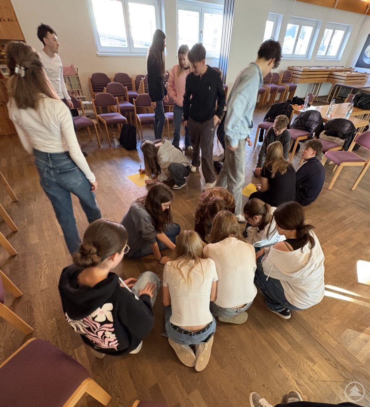 Bei kooperativen Spielen lernen die Jugendlichen, dass gemeinsame Lösungen oft nur durch Teamarbeit möglich sind. Jugendliche stehen im Kreis im Freien und halten verschiedenfarbige Schnüre, die in der Mitte zusammenlaufen. Gemeinsam versuchen sie, mit den Fäden Holzklötze zu bewegen und so eine Aufgabe zu lösen.