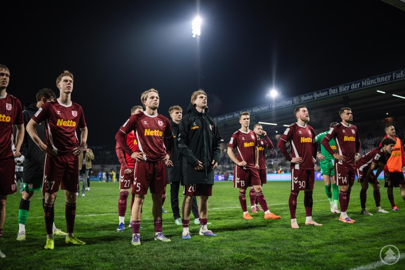 Mehrere Spieler des SSV Jahn Regensburg stehen nach dem Spiel auf dem Platz und blicken ersch&ouml;pft Richtung Trib&uuml;ne.