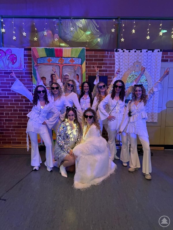 Die Garde Grafenau begeisterte mit ihren neuen Showkostümen in Weiß. Die Tänzerinnen der Garde posieren in weißen Bühnenoutfits mit Sonnenbrillen vor einer bunt dekorierten Kulisse.