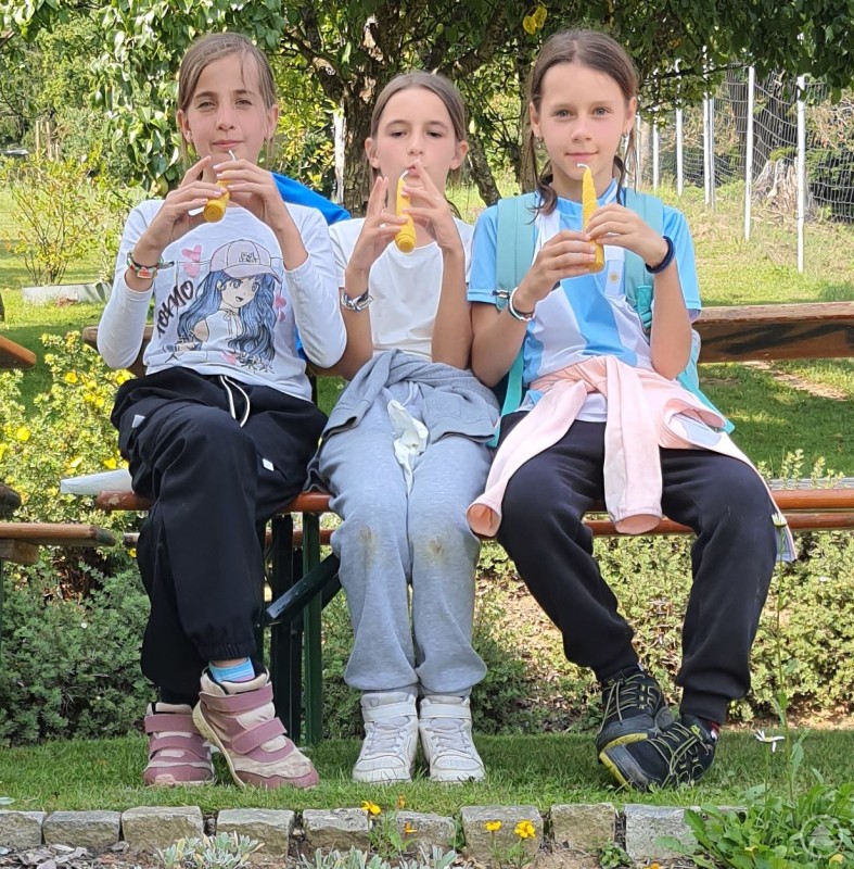 Drei Kinder sitzen auf einer Bank und essen Eis.