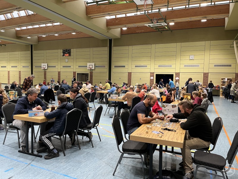 Ein Tag für alle Generationen: Der Spieletag in Grafenau begeisterte Hunderte Besucherinnen und Besucher. Zahlreiche Menschen unterschiedlichen Alters sitzen an Tischen in einer großen Turnhalle und spielen gemeinsam Brettspiele.