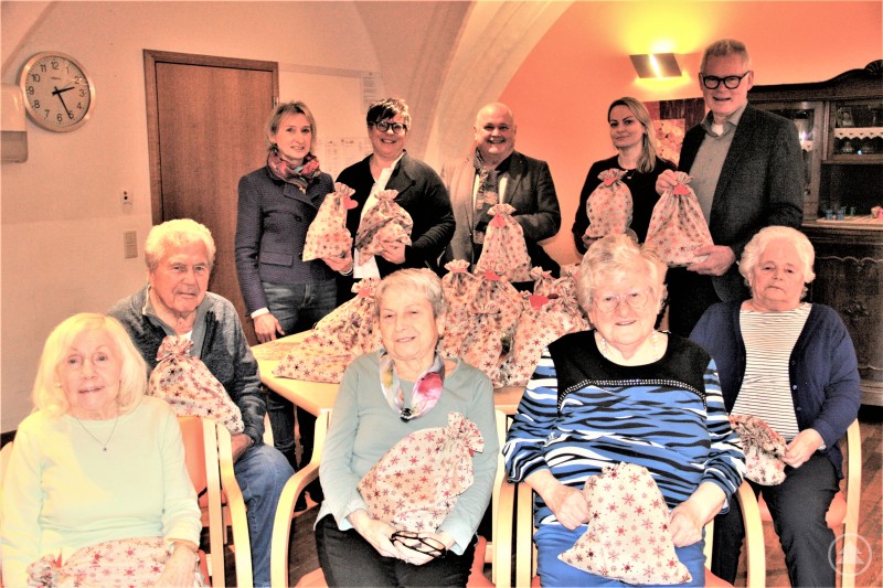 Stellvertretend für alle Bewohner des Heiliggeiststiftes in Passau freuten sich die Beiratsmitglieder des Seniorenstiftes Heilig (sitzend von links Annemarie Pfeil, Max Gruber, Katharina Öller, Christina Scherl und Brigitte Frankenberger zusammen mit Einrichtungsleiterin Rinata Deibele (stehend 2. v. r.) über die Geschenke aus der Wunschbaumaktion, überreicht durch Rotary-Präsidentin Caroline Schober (stehend 2.v.l.) sowie (v.l.) Marianne und Herbert Krammer und Helmuth Rücker überreicht wurden. Mehrere Seniorinnen und Senioren sitzen und stehen gemeinsam mit Vertreterinnen und Vertretern des Rotary-Clubs Passau-Dreiflüssestadt in einem Gemeinschaftsraum des Heiliggeiststifts in Passau und halten Geschenktaschen aus der Wunschbaumaktion in den Händen.