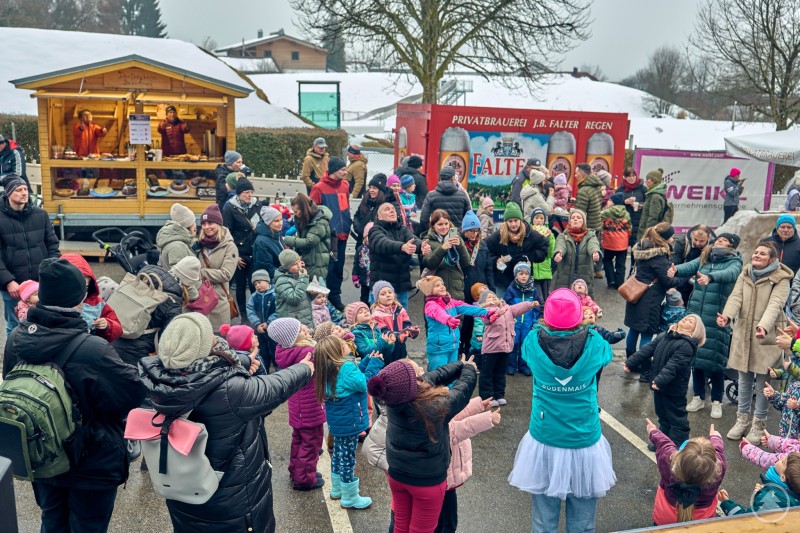 Große Begeisterung beim Kinderprogramm rund um den ArberBlitz in Bodenmais – zahlreiche Familien verfolgten das bunte Treiben. Viele Kinder und Erwachsene stehen dicht beieinander auf einem Platz in Bodenmais. In der Mitte animiert eine Betreuerin Kinder zu gemeinsamen Bewegungen. Im Hintergrund sind Marktstände und zahlreiche Zuschauer zu sehen.