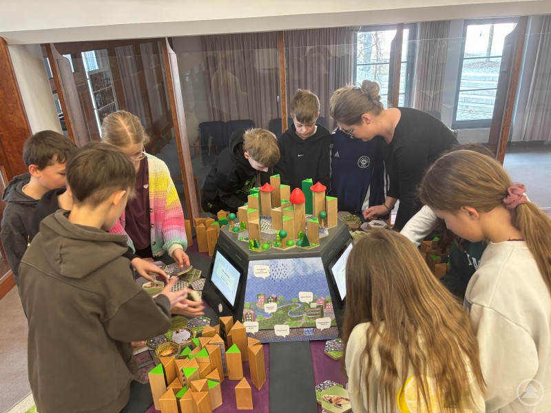 Rund 400 Schülerinnen und Schüler aus den Grundschulen des Landkreises (hier Kinder der Grundschule Böhmzwiesel) konnten sich in der Ausstellung spielerisch mit aktuellen Herausforderungen rund um Wasser auseinandersetzen. Mehrere Grundschulkinder stehen gemeinsam um eine interaktive Station und beschäftigen sich mit einem Modell einer Stadtlandschaft, bei dem sie spielerisch Aufgaben rund um Wasser lösen.