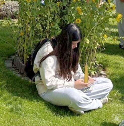 Ein Mädchen sitzt im Gras, lehnt am Baum und schreibt in ein Heft.