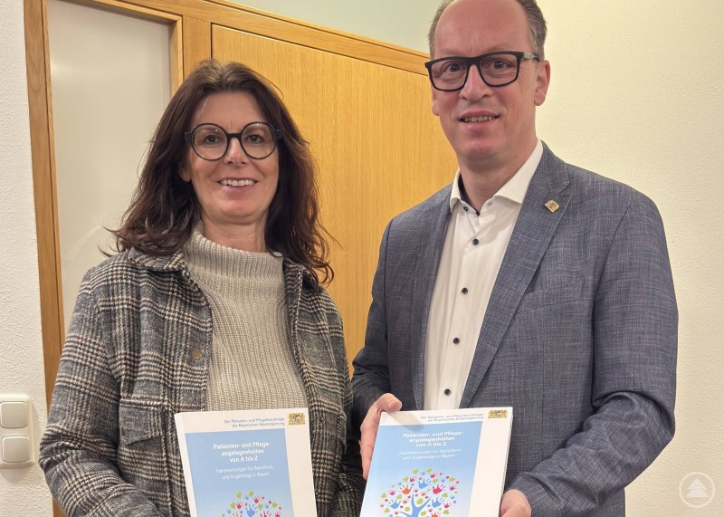 MdL Martin Behringer nutzte die Gelegenheit der Übergabe, um zugleich ergänzend auf einen kostenlosen Bestellservice hinzuweisen. Ein Mann und eine Frau stehen in einem Büro nebeneinander und halten jeweils ein Exemplar eines Ratgebers zu Patienten und Pflegeangelegenheiten der Bayerischen Staatsregierung in der Hand.