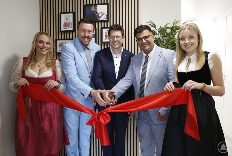Die Mitarbeiterinnen Pia Aulinger (r.) und Pia Friedl (l.) durften das Eröffnungsband spannen, das Kefah Alazzam (2.v.r.) und Imrich Rajec jun. (2.v.l.) zusammen mit Bürgermeister Martin Pichler durchschnitten. Fünf Personen stehen nebeneinander vor einem modernen Eingangsbereich und durchschneiden gemeinsam ein rotes Eröffnungsband. Sie sind festlich gekleidet und lächeln in die Kamera.