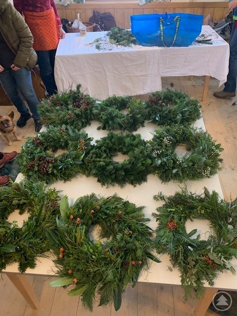 Auf einem Tisch liegen zahlreiche frisch gebundene Adventskränze, alle individuell gestaltet mit Tannenzweigen, Beeren, Zapfen und verschiedenem Naturmaterial.