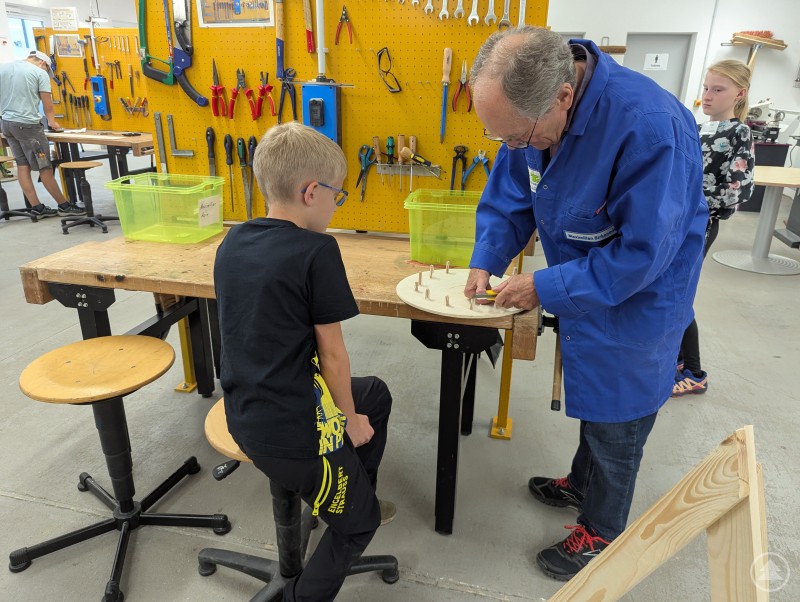 TfK-Mentor hilft Kind dabei, ein Glücksrad aus Holz zu verschrauben