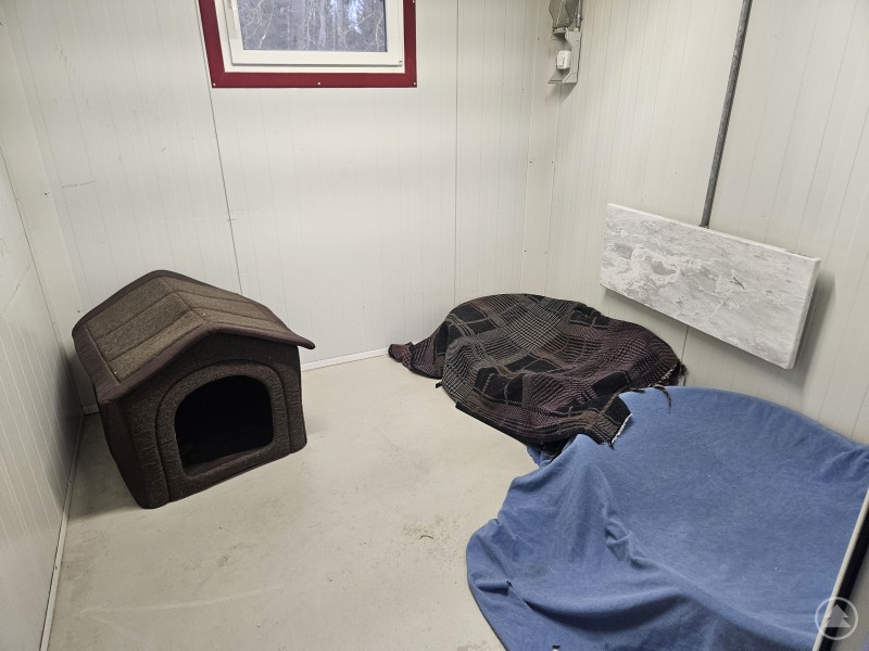 Ein sauberer, schlichter Raum mit Hundeh&uuml;tte, Decken und Liegepl&auml;tzen. Der Bereich wirkt wie eine ruhige Unterbringung f&uuml;r Tiere, z. B. in einem Tierheim.
