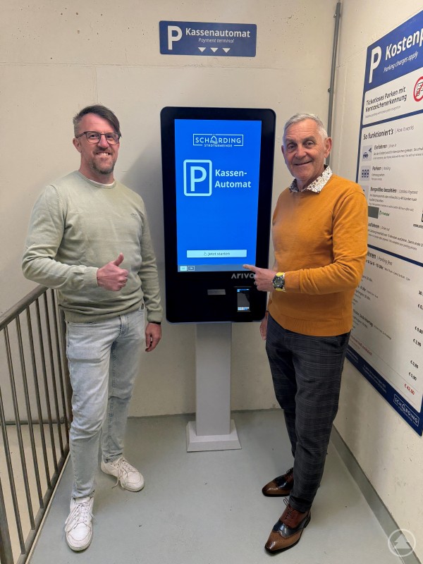 Vorstellung des neuen digitalen Kassensystems im Parkhaus Schärding. Zwei Männer stehen neben einem modernen Parkautomaten mit Touchscreen und zeigen auf das Display in einem Parkhaus.
