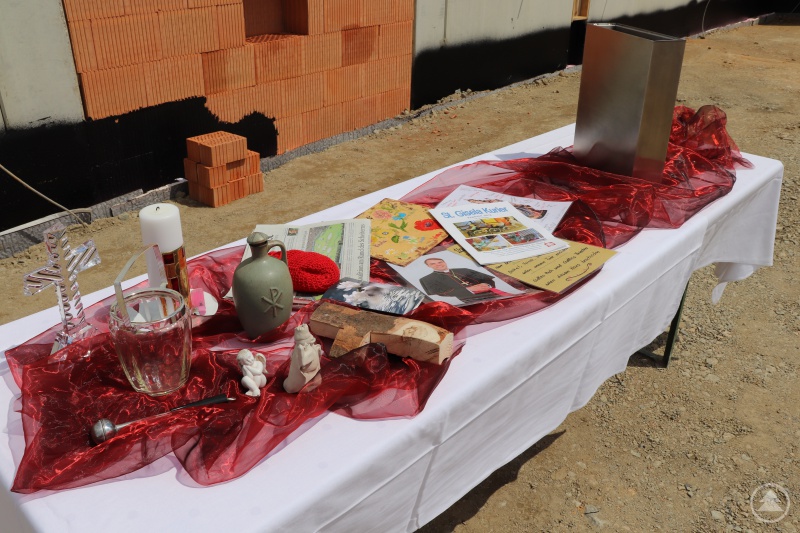 Die Zeichen der Bewohnerinnen und Bewohner im Grundstein: Ein Kreuz, das sie aus Holz vom Karoli-Wald gefertigt haben, eine Tonfigur der Namenspatronin St. Gisela sowie Segenswünsche. Dazu legten sie für die Gegenwart aktuelle Münzen, ein Bild von Diözesanbischof Stefan Oster, die Tageszeitung und die Hauszeitschrift, den St. Gisela-Kurier.