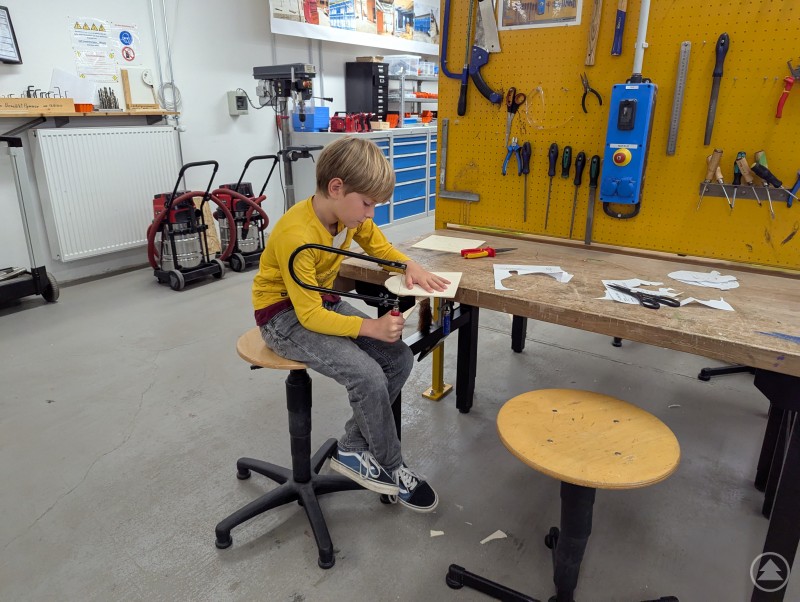 Kind sägt Holzstück an einer Werkbank aus