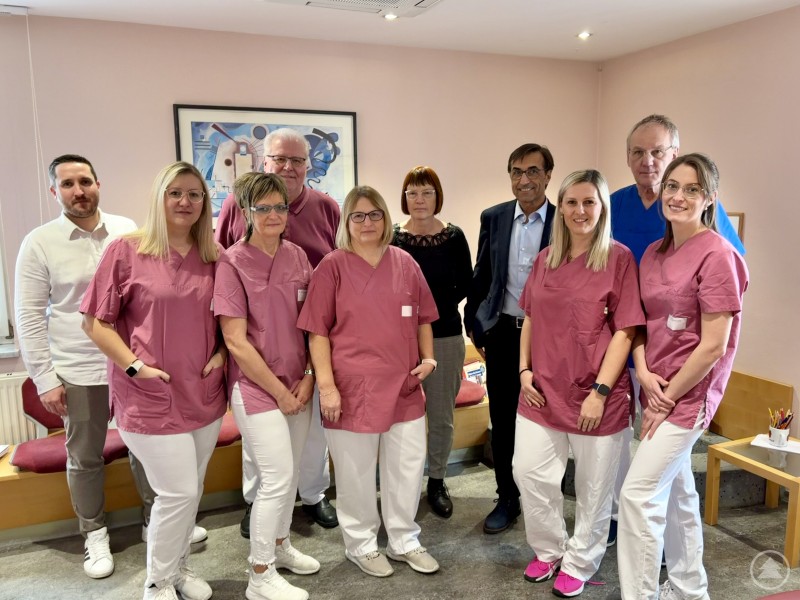 Das Team des MVZ Grafenau begrüßt Dr. med. Michael Eckstein als neuen Facharzt für Hals-Nasen-Ohrenheilkunde. Eine Gruppe aus medizinischem Fachpersonal in rosa Kasacks sowie mehrere Ärzte stehen gemeinsam in einem Behandlungsraum und blicken in die Kamera.