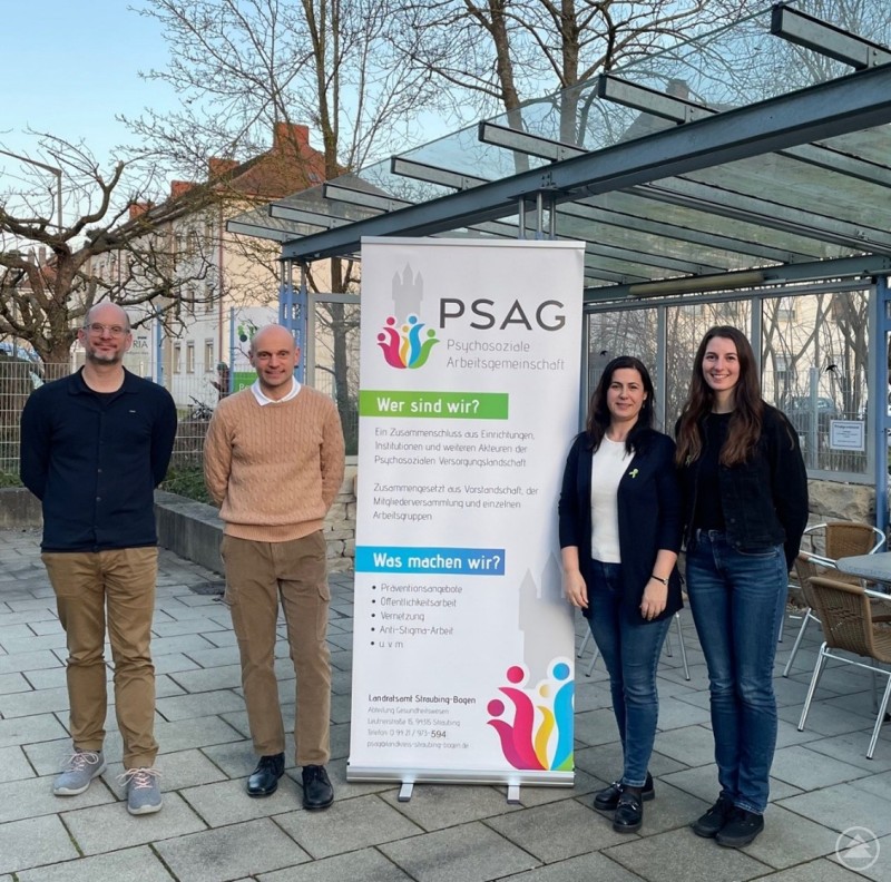 Valentin Stollberg (PSAG Vorstand, BTZ-VdK Rehawerk Straubing), Ernest Fischmann (Facharzt für Psychiatrie am Gesundheitsamt Straubing-Bogen), Luisa Hammerschmied (1. Vorsitzende PSAG, Moderation, BRK Sozialpsychiatrischer Dienst Straubing) und Christina Drexler (PSAG Geschäftsführung am Gesundheitsamt Straubing-Bogen, von links). Vier Personen stehen vor einem Roll-up der Psychosozialen Arbeitsgemeinschaft (PSAG) und informieren über ihre Arbeit im Bereich der psychischen Gesundheit.