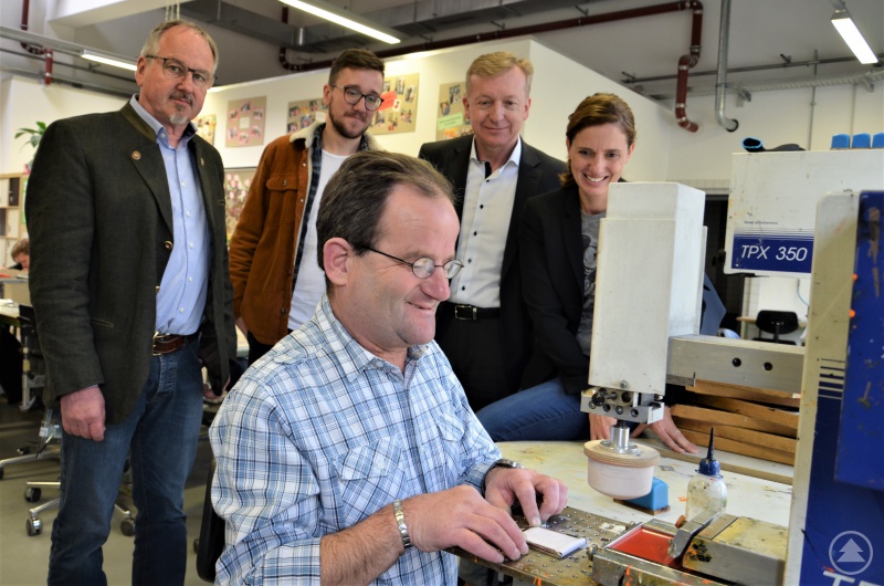 Mitarbeiter Reinhard (sitzend) aus Tiefenbach zeigt wie er die Buntstifte-Verpackung mit dem Label der Stiftung Kinderlächeln bedruckt hat – (hinten v.l.) der stellvertretende Einrichtungsleiter Bernhard Gayer, Michael Wallner, Dr. Josef Sonnleitner und Dr. Maria Diekmann.