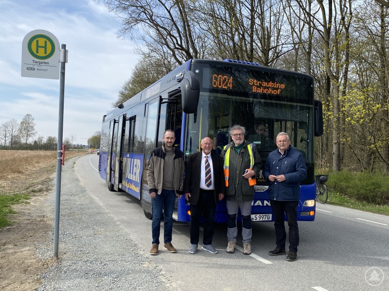 Wiesen noch einmal auf die Möglichkeit hin, mit dem ÖPNV zum Tiergarten zu kommen: Ludwig Fischer (Stellvertr. Direktor Tiergarten), 3. Bürgermeister Werner Schäfer, Johann Meindorfer und Landrat Josef Laumer (von links). Das Bild zeigt die neu eingerichtete Bushaltestelle „Tiergarten“ in ländlicher Umgebung. Vor einem Bus der Linie 6024 nach Straubing Bahnhof stehen vier Männer, vermutlich Vertreter des Verkehrsunternehmens oder der Kommune, zur Einweihung oder offiziellen Besichtigung. Der Bus trägt die Aufschrift „MÜLLER“, im Hintergrund sind Felder und Wald zu sehen.