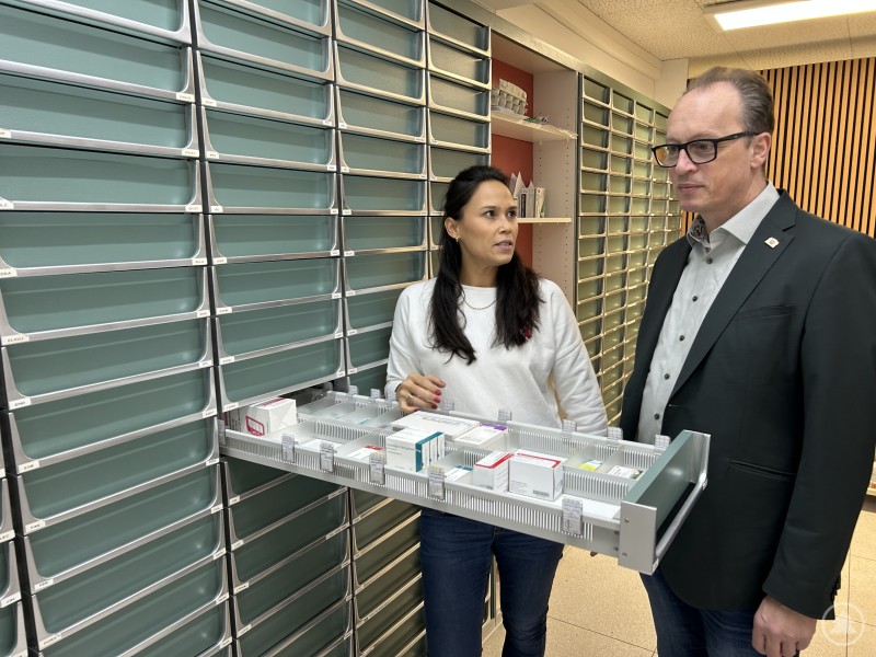 Elena Pleintinger hat gerade in noch mehr Service vor Ort investiert und einen Abholautomaten installieren lassen, wie sie MdL Martin Behringer erklärte. Aber wenn die Einnahmen weiter hinter Kosten zurückbleiben, hilft selbst schneller als eine Online-Apotheke vielleicht auch nicht mehr. Eine Apothekerin steht gemeinsam mit einem Politiker in einem Apothekenlager. Die Frau hält eine geöffnete Medikamentenschublade in den Händen und erklärt etwas, während der Mann aufmerksam zuhört. Im Hintergrund sind zahlreiche beschriftete Medikamentenschränke zu sehen.