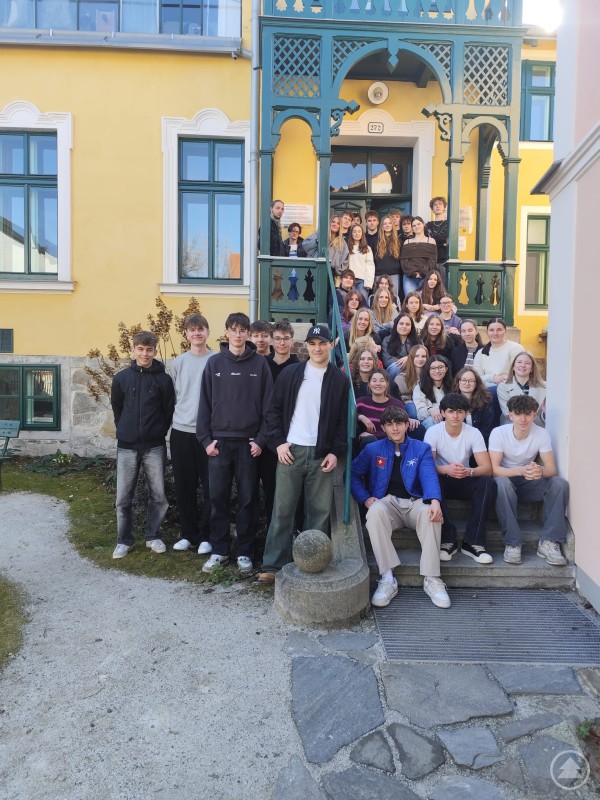 Eine gro&szlig;e Gruppe Jugendlicher sitzt und steht auf einer Treppe vor einem historischen Geb&auml;ude und posiert f&uuml;r ein Gruppenfoto.