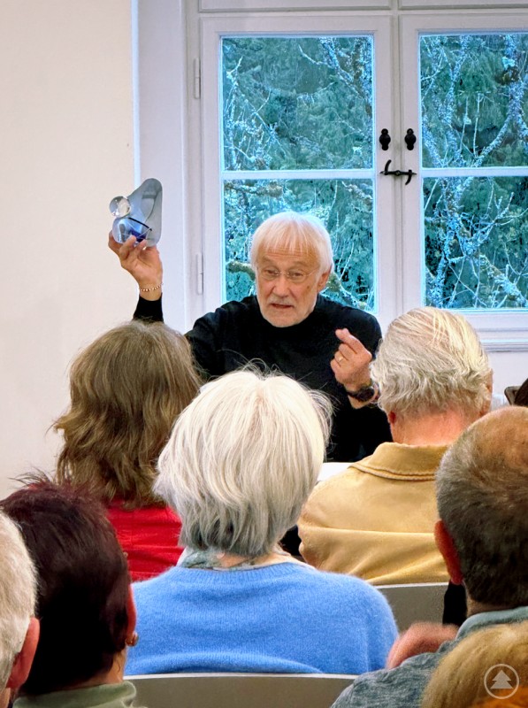 Karl-Heinz Reimeier bei seiner Lesung in der Galerie Wolfstein. Karl-Heinz Reimeier hält ein gläsernes Kunstobjekt hoch und spricht zu seinem Publikum.