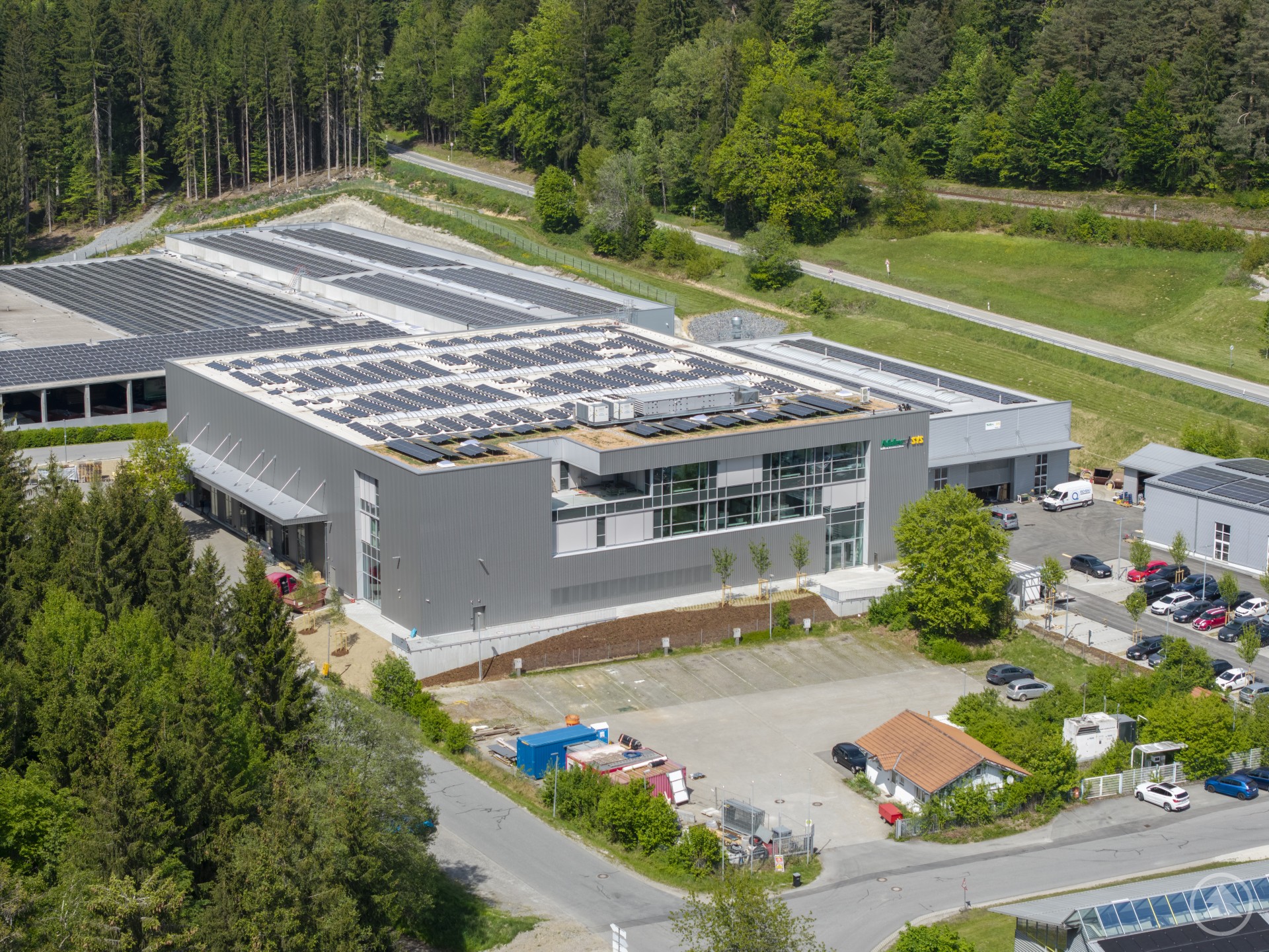 Der neue Standort aus der Vogelperspektive – mit Photovoltaikanlage und viel Platz für Innovation. Luftaufnahme des Nidec SYS Firmenareals mit Gebäudekomplex, Solaranlage und umgebender Natur.