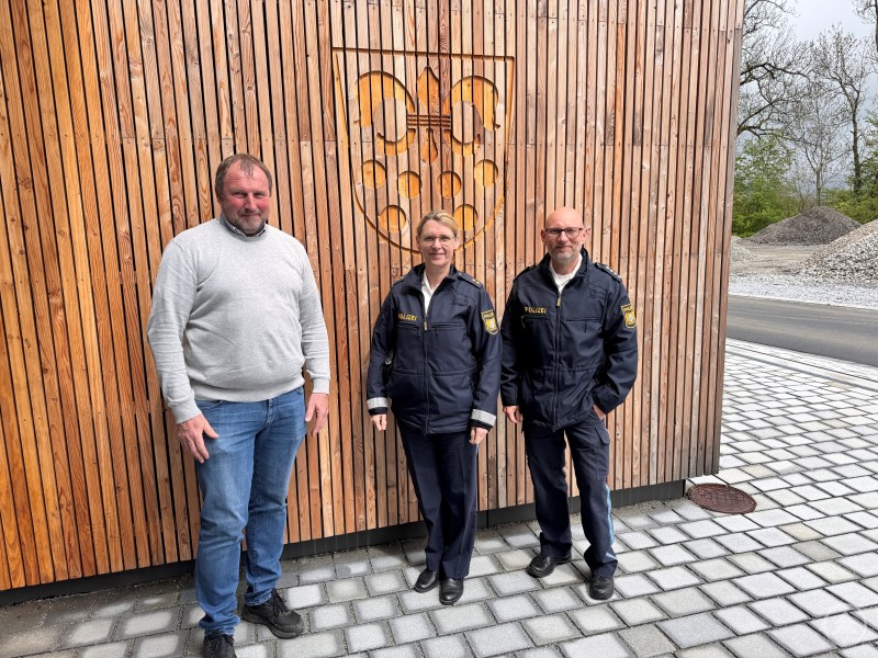 Stolz führte Bgm. Roland Freund die Polizeiführung PORin Ingrid Grötzinger und PHK Georg Binder durchs frisch renovierte Rathaus Drei Personen – ein Mann in Zivilkleidung und zwei Polizisten – stehen vor einer modernen Holzfassade mit eingraviertem Gemeindewappen.