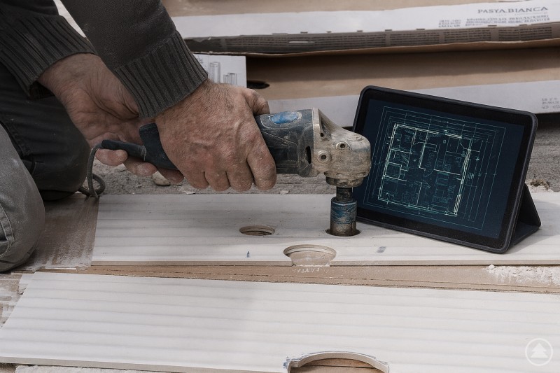 Digitalisierung im Handwerk: Moderne Technologien unterstützen traditionelle Arbeitsweisen. Eine Person arbeitet mit einer elektrischen Bohrmaschine an einer Holzplatte, während daneben ein Tablet mit einem digitalen Bauplan steht. Im Hintergrund liegen Baumaterialien und Werkzeuge.