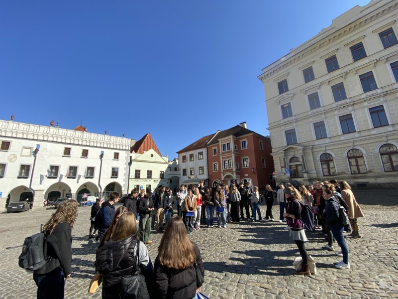 Bei einer Stadtführung setzten sich die Jugendlichen mit der Geschichte von Český Krumlov auseinander. Jugendliche stehen in einem großen Kreis auf einem historischen Marktplatz und hören einer Person zu, die etwas erklärt.