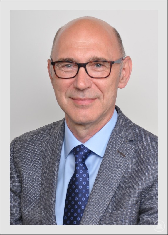 Dr. med. Hendryk Kalbarczyk, Facharzt für Neurochirurgie. Porträt eines Mannes mit Brille im Anzug vor neutralem Hintergrund.