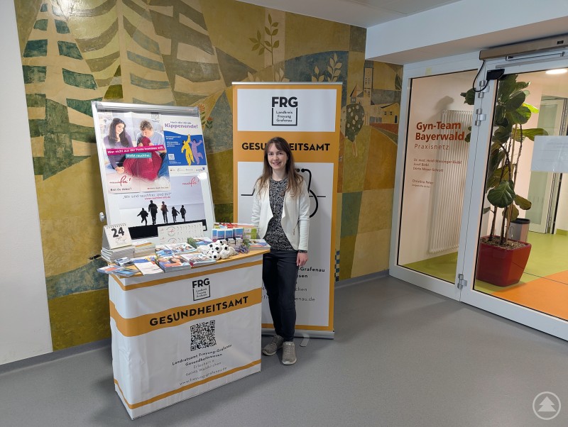 Dr. med. Karin Drachsler am Infostand im Gesundheitszentrum mit Informationsmaterialien und Giveaways rund um den Rauchstopp sowie zur Aktion Rauchfrei im Mai. Eine Frau steht an einem Informationsstand des Gesundheitsamtes mit Broschüren und Materialien zum Thema Rauchstopp im Eingangsbereich eines Gesundheitszentrums.
