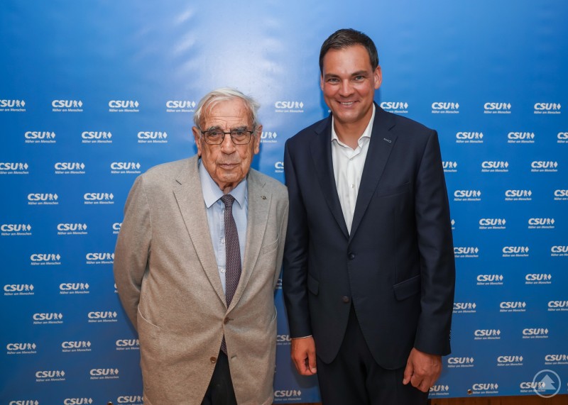 Sebastian Gruber (rechts) mit einem Unterstützer nach der erfolgreichen Nominierung zum Landratskandidaten der CSU. Sebastian Gruber posiert mit einem älteren Herrn vor einer CSU-Fotowand.