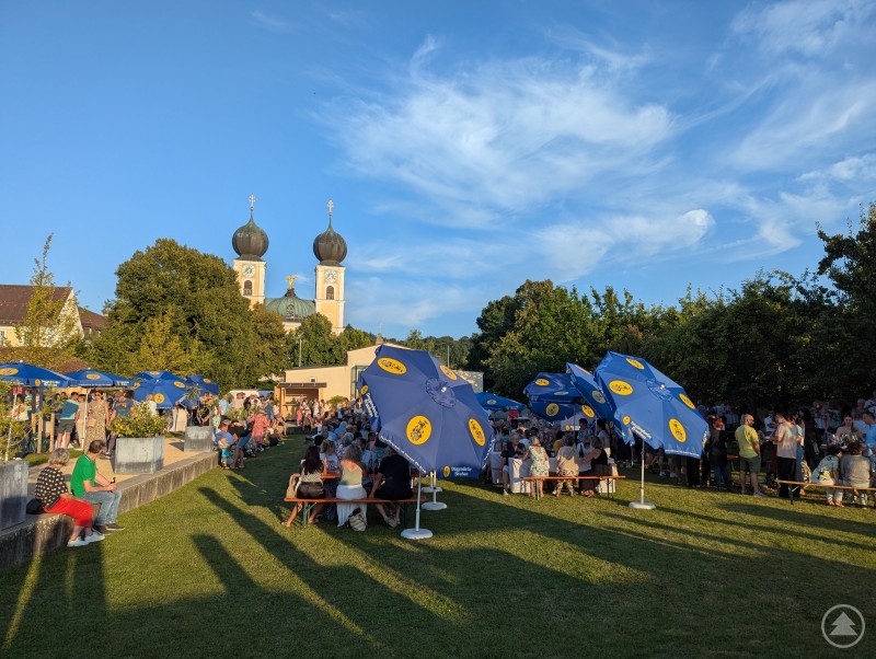 Im Prälatengarten Metten traf italienisches Dolce Vita auf bayerische Geselligkeit Prälatengarten Metten mit Bierbänken und Sonnenschirmen vor der Kirche St. Michael
