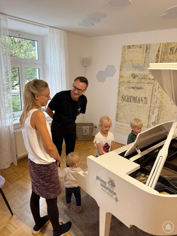 Kinder und Mutter stehen mit Klavierlehrer am weißen Flügel