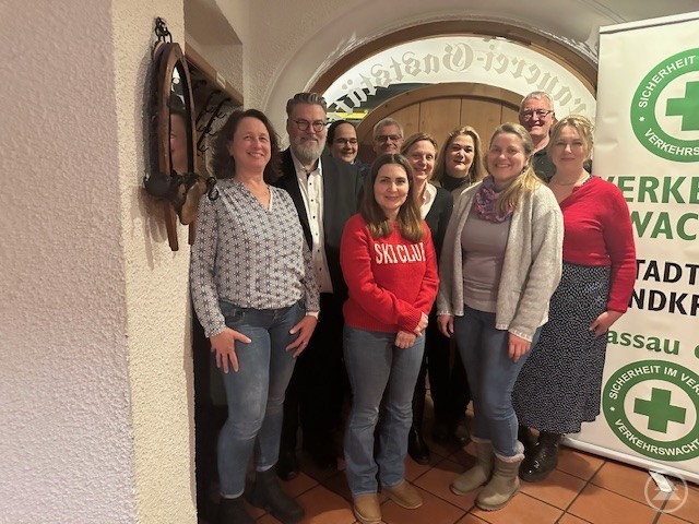 Anerkennung und Lob von höchster Stelle – von links: POK’in Doris Meth, Bürgermeister Andreas Rother, 2. v. re. Jörg Wittkowski und die ehrenamtlichen Schulweghelfer. Gruppenfoto von ehrenamtlichen Schulweghelfern, Bürgermeister Andreas Rother, Polizei und Verkehrswacht. Die Gruppe steht lächelnd im Eingangsbereich eines Gebäudes, rechts ein Roll-up der Verkehrswacht Passau.