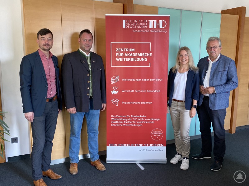 Prof. Dr. Wolfgang Dorner, Wirtschaftsförderer Martin Köck, Corina Welsch und Landrat Josef Laumer (von links) beim Termin zur Vorstellung der Weiterbildungsangebote der TH Deggendorf. Vier Personen stehen neben einem roten Informationsrollup des Zentrums für Akademische Weiterbildung der TH Deggendorf in einem Büro.