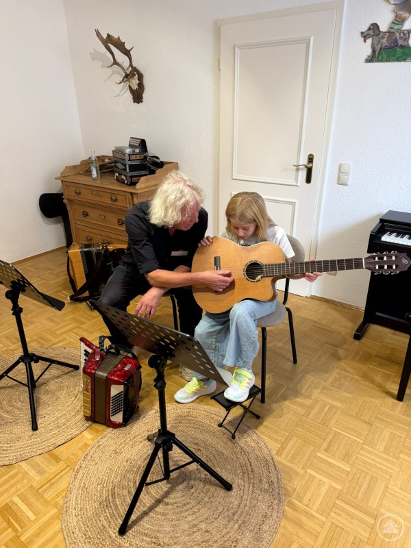 Gitarrenlehrer zeigt Schülerin einfache Griffe an der akustischen Gitarre